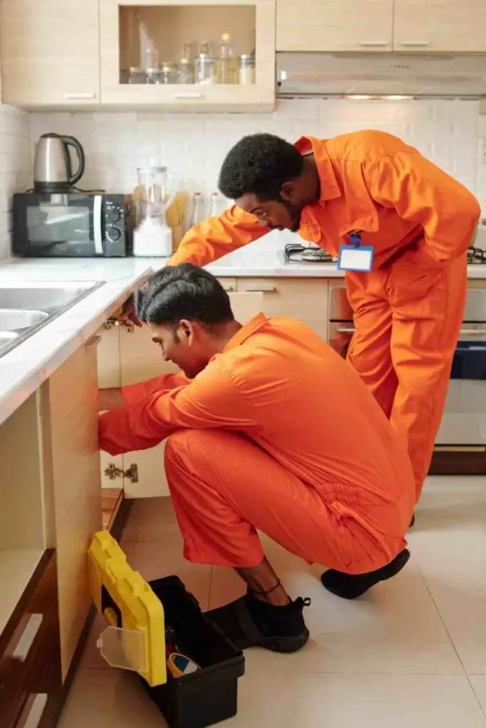 Plumbers checking pipework beneath a kitchen sink during an emergency enquiry in Burpham