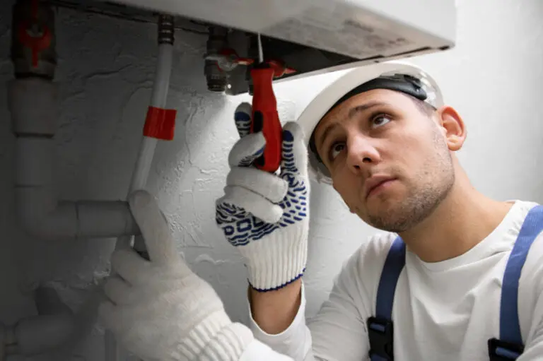 Engineer checking accessible valves and pipework beneath a heating appliance