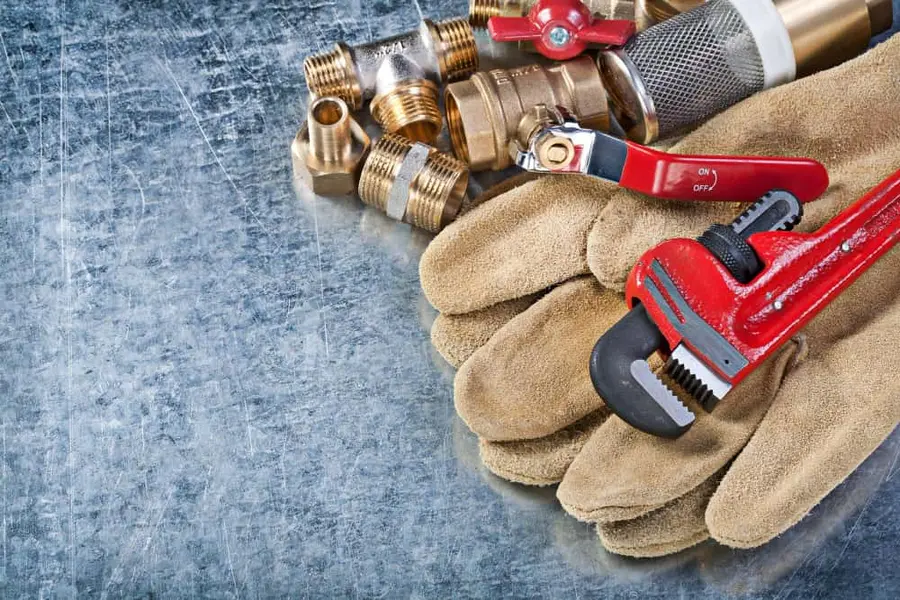 Plumbing fittings, isolation valve, gloves and pipe wrench prepared for a leak investigation