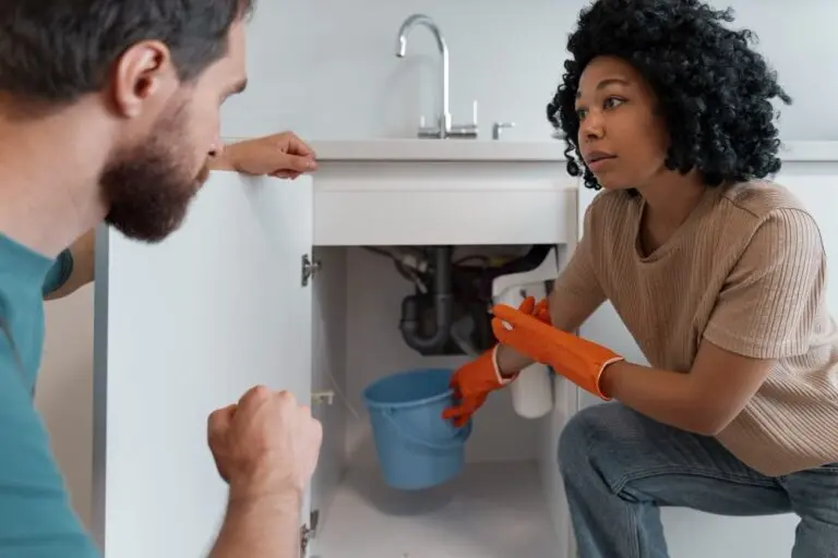 Plumber discussing an accessible leak beneath a kitchen sink with a homeowner