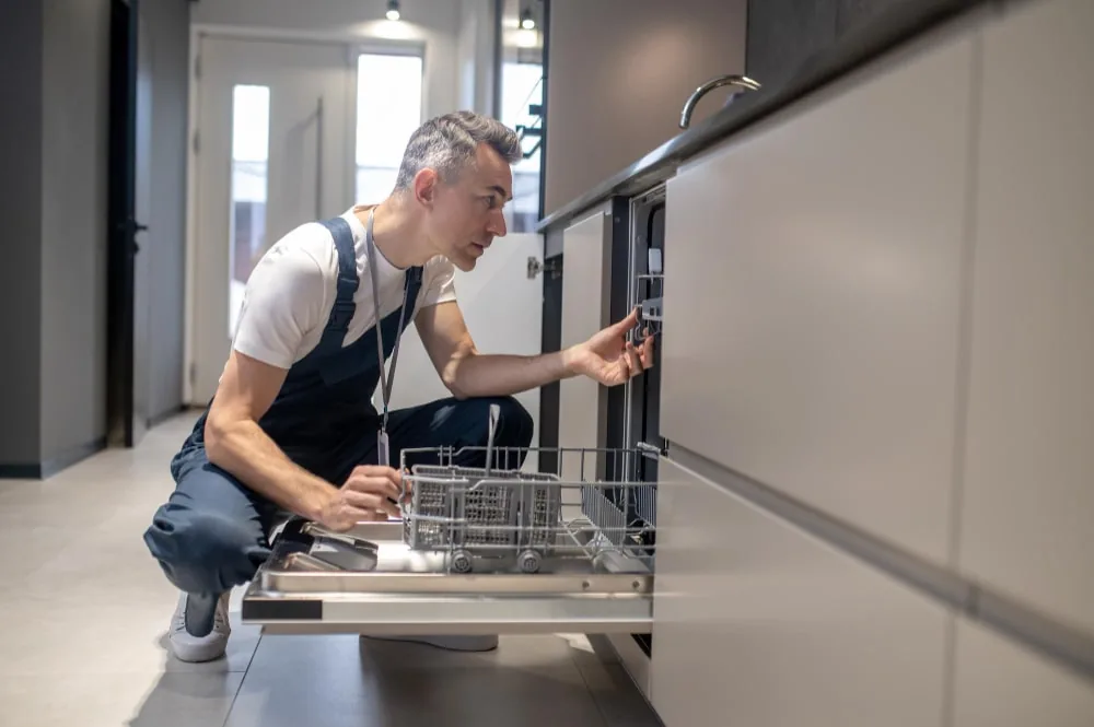 Plumber inspecting an open integrated dishwasher in a kitchen