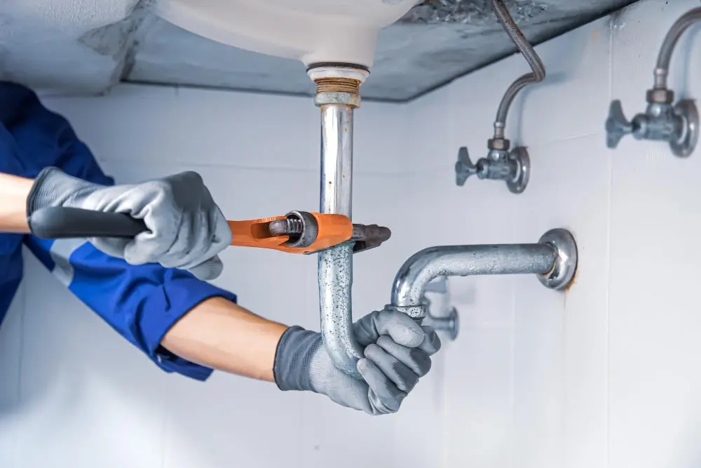 Plumber using a wrench to repair waste pipework beneath a sink