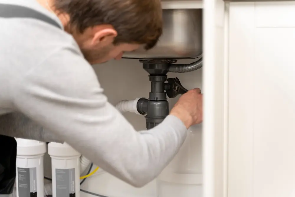 Plumber working on accessible pipework beneath a kitchen sink