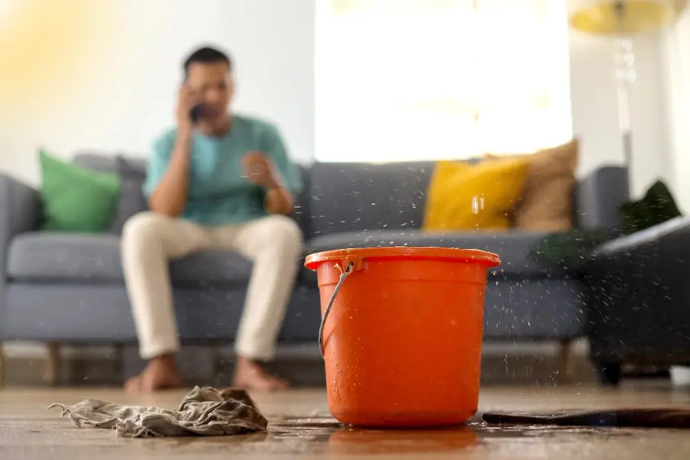Bucket collecting water from an active ceiling leak while a homeowner calls for help